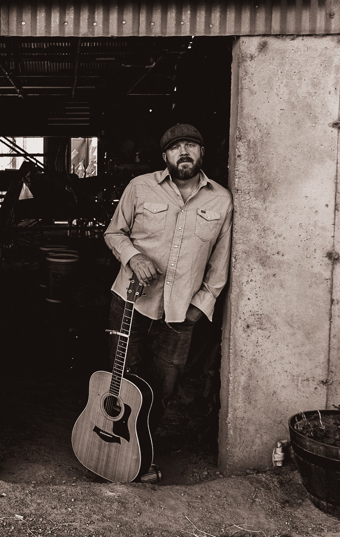 Everett Rogers leaning in a barn doorway with an acoustic guitar