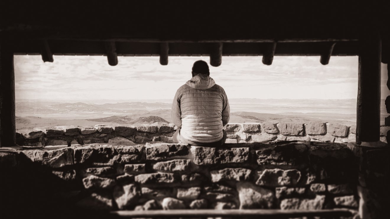 A figure sitting alone in a stone shelter, looking out over open country