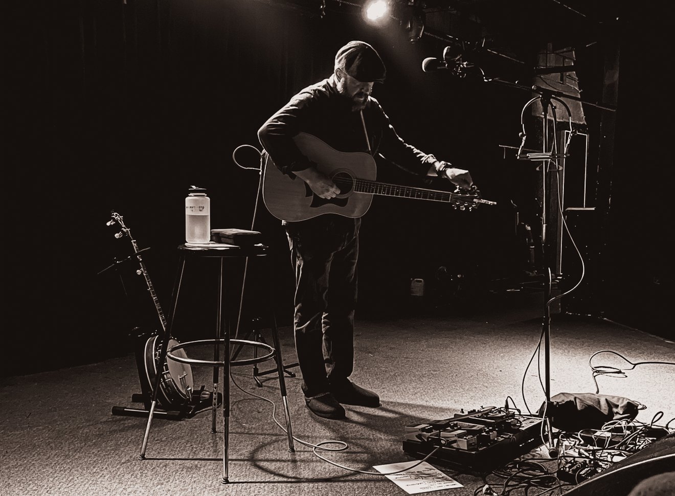 Everett Rogers alone on a dark stage, tuning a guitar beside a banjo and a stool