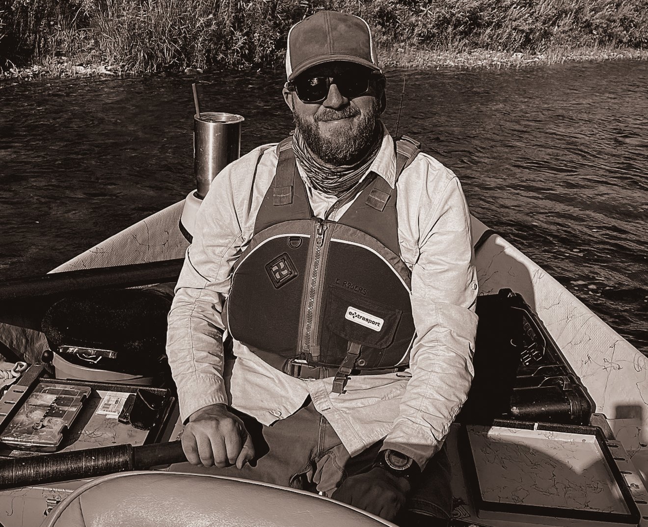 Everett Rogers at the oars of a drift boat, river running behind him